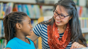 A teacher and a child smiling at each other over a book